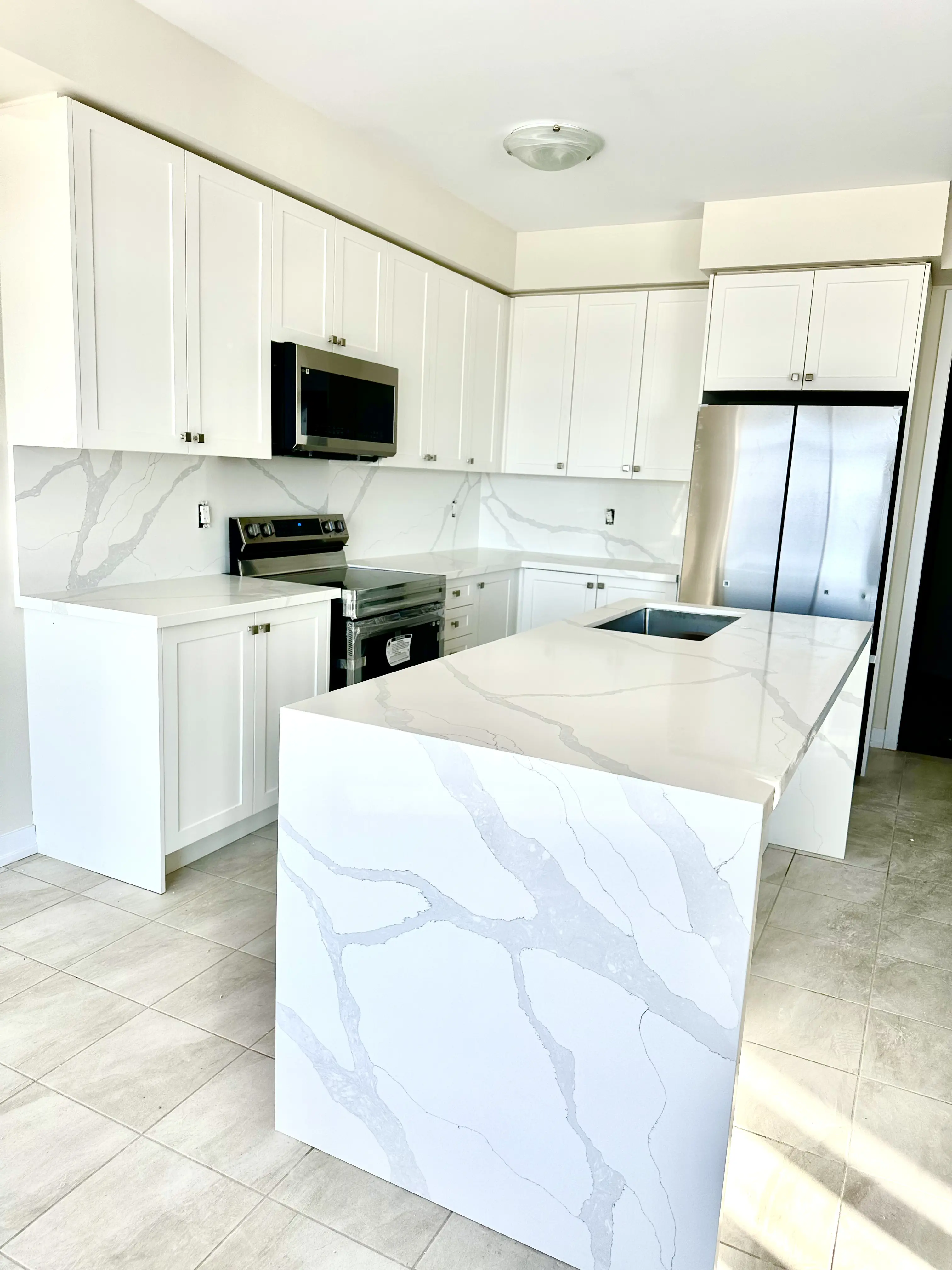 White kitchen island with a veined stone waterfall end and matching backsplash